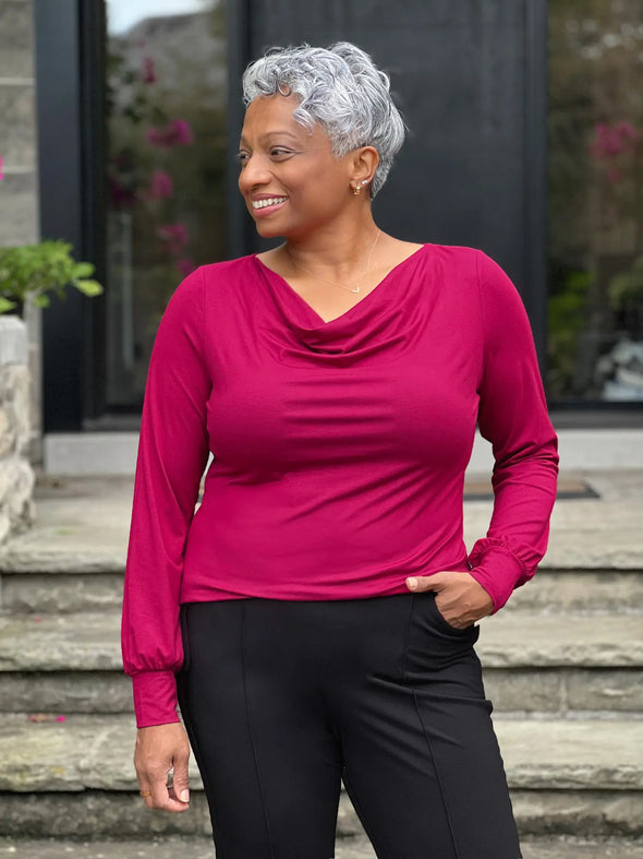 Miik model Keethai (5'5", medium) smiling and looking away wearing Miik's  Devina draped cowl neck long sleeve top in cerise, regular fit, with a dress pant in black 