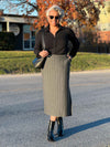 Woman smiling wearing Miik's Devon midi skirt in granite pinstripe with a collared black top and matching colour boots and purse