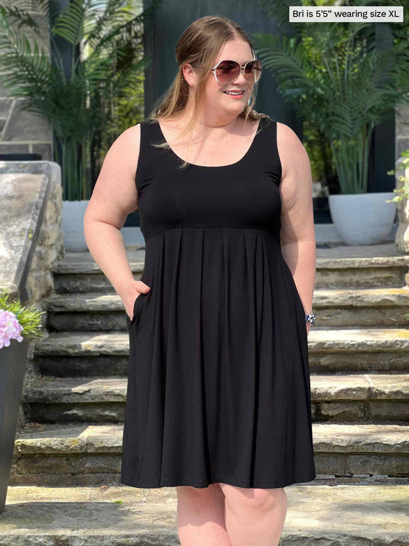 Miik model Bri (5'5", xlarge) smiling and looking away wearing Miik's Ela pleated reversible pocket dress in black