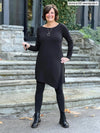 Miik founder Donna (5'6", small) smiling wearing Miik's Elsie asymmetrical long sleeve tunic in black with a legging and boots in the same matching colour #color_black