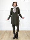 Miik founder Donna (5'6", small) smiling while standing in front of a white wall wearing Miik's Elsie asymmetrical long sleeve tunic in olive with a matching colour legging, black boots and a scarf #color_olive 