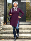 Miik model Keethai (5'5", medium) smiling wearing Miik's Elsie asymmetrical long sleeve tunic in port, jeans, a printed scarf and a black purse #color_port