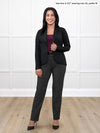 Miik model Yasmine (5'0", xsmall, petite) smiling while standing in front of a white wall wearing Miik's Emily soft blazer in black, petite fit, with a charcoal dress pant, a black belt and heels and a port tank top #color_black