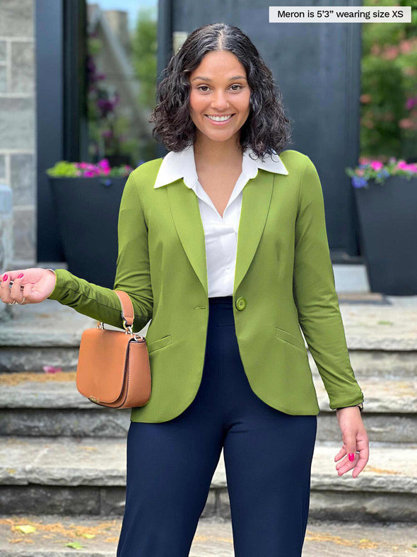 Miik model Meron (5'3", xsmall) smiling wearing a collared shirt in white, a navy pant and Miik's Emily soft blazer in green moss