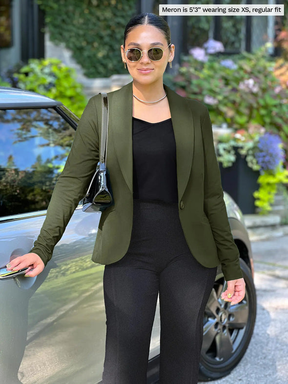 Miik model Meron (5'3", xsmall) standing next to a car wearing an all black outfit along with Miik's Emily soft blazer in olive, regular fit #color_olive