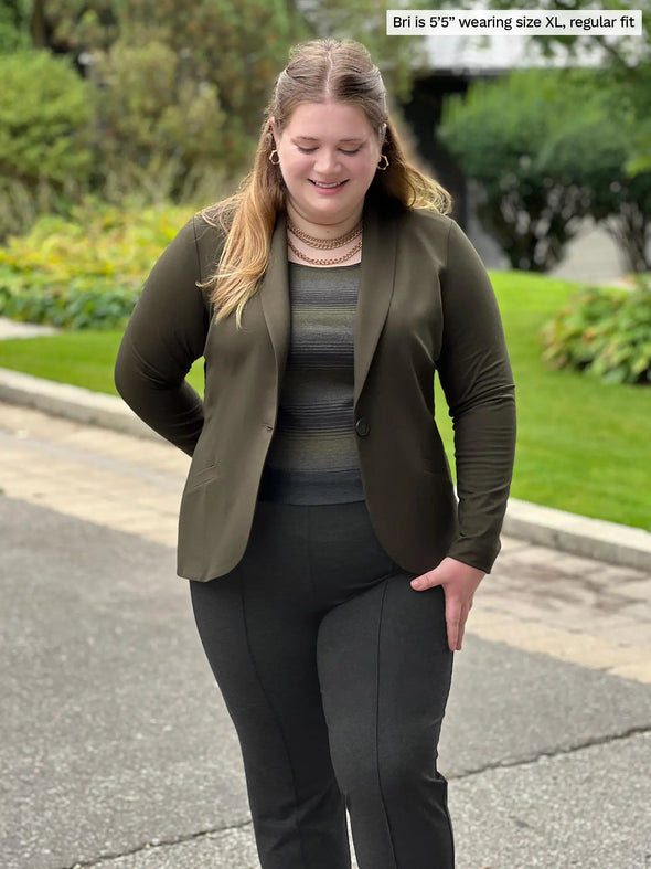 Miik model Bri (5'5", xlarge) looking down and smiling wearing Miik's Emily soft blazer in olive, regular fit, with a charcoal dress pant and a striped shirt 
#color_olive