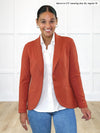 Miik model Meron (5'3", xsmall) smiling wearing Miik's Emily soft blazer in paprika, regular fit, with a collared shirt in white and jeans #color_paprika-melange 