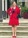 Miik model Christal (5'3", medium) smiling wearing Miik's Emily soft blazer in poppy red with a flouncy skirt in the same colour and a navy tank
