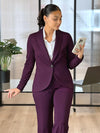 Miik model Meron 95'3", xsmall) looking down at her phone while leaning against to a office desk wearing Miik's Emily soft blazer in port with a wide leg pant in the same matching colour and a collared white shirt #color_port 
