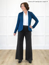 Miik founder Donna (5'6", small) standing in front of a white wall wearing a collared shirt in white, Miik's Emily soft blazer in teal, regular fit, and a wide leg pant in black #color_teal