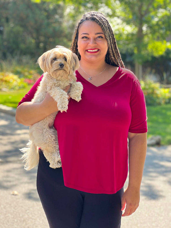 Miik plus size Sarita (5'7", 2x) smiling while holding a puppy wearing Miik's Gracelyn v-neck classic tee in bordeaux 