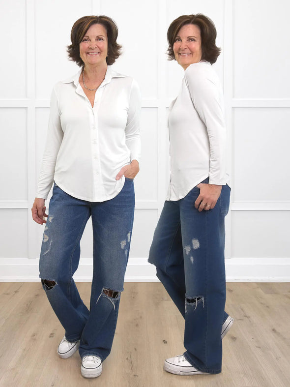 Miik founder Donna (5'6", small) smiling while standing in front of a white wall wearing Miik's Inna long sleeve button up shirt in white and ripped jeans. Donna's also showing the side details of the shirt. 
#color_white 