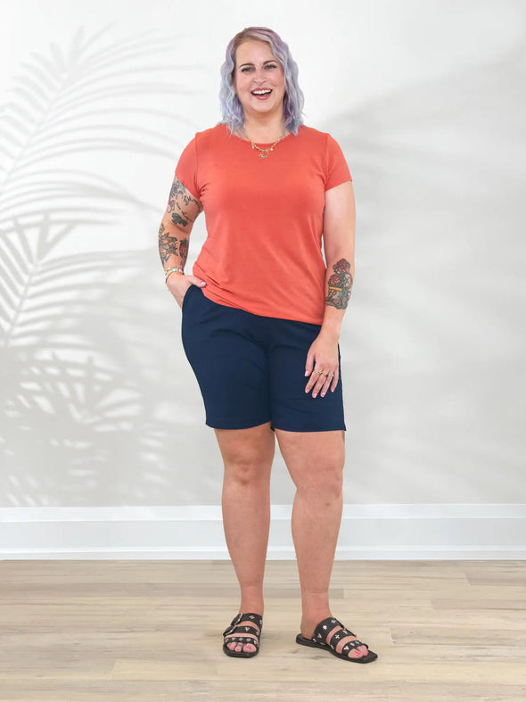 Miik model Kaitlin (5'9", xxlarge) smiling wearing a papaya melange tee along with Miik's Irelynn bermuda pocket short in navy