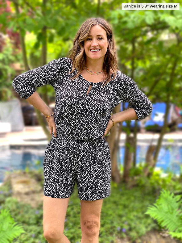Woman standing in nature with a pool in the background smiling and wearing Miik's Janice 3/4 sleeve short romper in black and white colour.