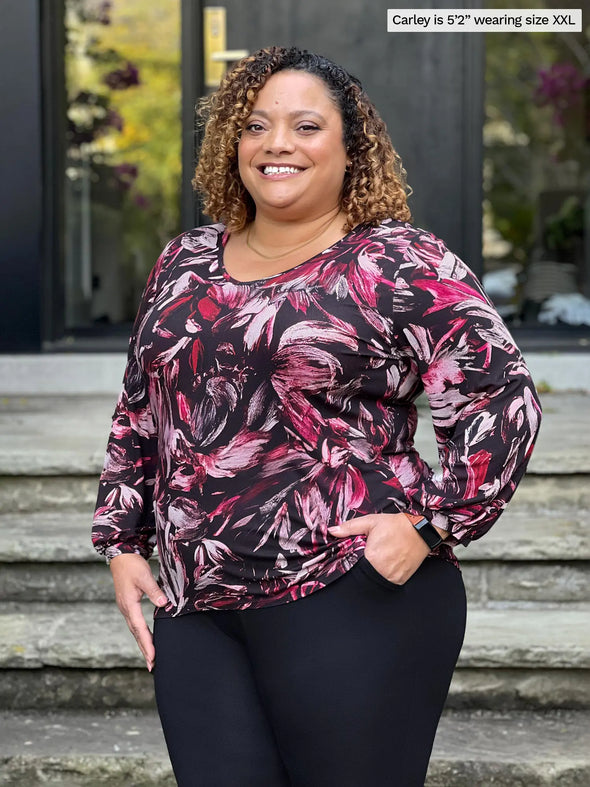 Miik model Carley (5'2", xxlarge) smiling wearing Miik's Jayna v-neck 3/4 sleeve top in midnight floral with a black dress pant #color_midnight-floral