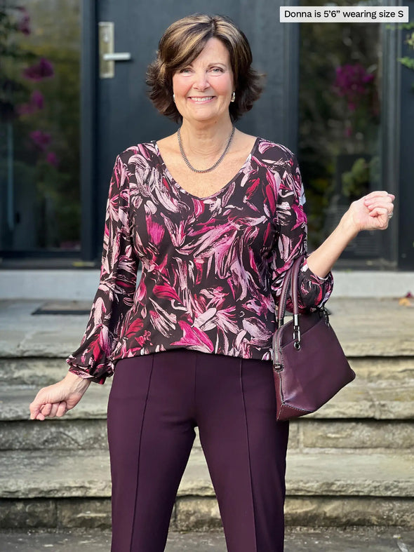 Miik founder Donna (5'6", small) smiling wearing a port dress pant along with Miik's Jayna v-neck 3/4 sleeve top in midnight floral #color_midnight-floral