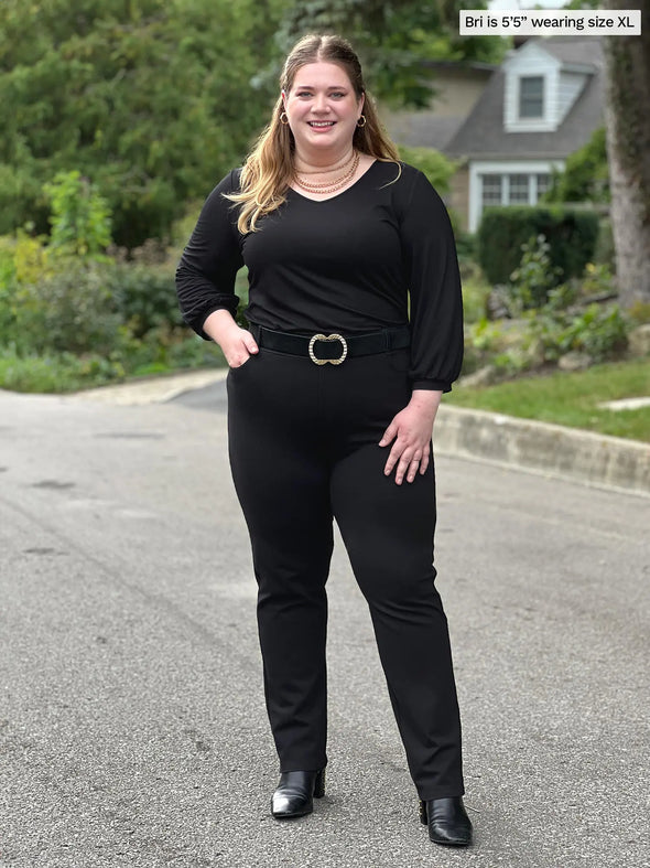 Miik model Bri (5'5", xlarge) smiling wearing an all black outfit: Miik's Jayna v-neck 3/4 sleeve top and a dress pant and a belt #color_black