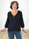 Miik founder Donna (5'6", small) smiling while standing in front of a white wall wearing Miik's Jayna v-neck 3/4 sleeve top in black with jeans 