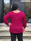 Miik model Marilyn (5’2”, medium) standing with her back towards the camera showing the back of Miik's Jayna v-neck 3/4 sleeve top in cerise #color_cerise