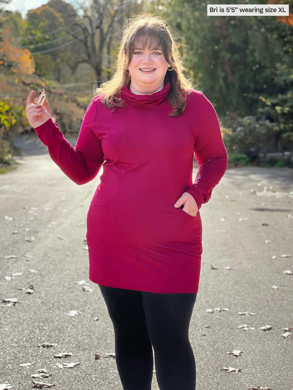 Miik model Bri (5'5", xlarge) smiling wearing Miik's Kaito cowl neck pocket tunic in cerise with black leggings #color_cerise 