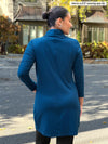 Miik model Meron (5’3”, xsmall) standing with her back towards the camera showing the back of Miik's Kaito cowl neck pocket tunic in teal #color_teal 