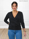 Miik model Meron (5’3”, xsmall) wearing Miik's Kathryn ruched faux-wrap blouse in black with blue jeans #color_black