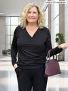 Miik model Carolyn (5'10", large) smiling wearing Miik's Kathryn ruched faux-wrap blouse in black with a pant in the same colour and a port purse #color_black