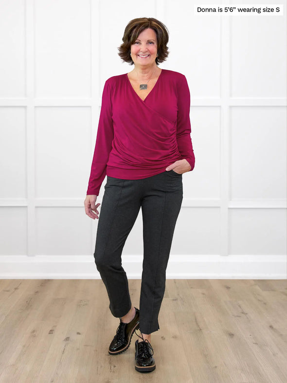 Miik founder Donna (5'6", small) smiling while standing in front of a white wall wearing Miik's Kathryn ruched faux-wrap blouse in cerise with a charcoal dress pant #color_cerise 