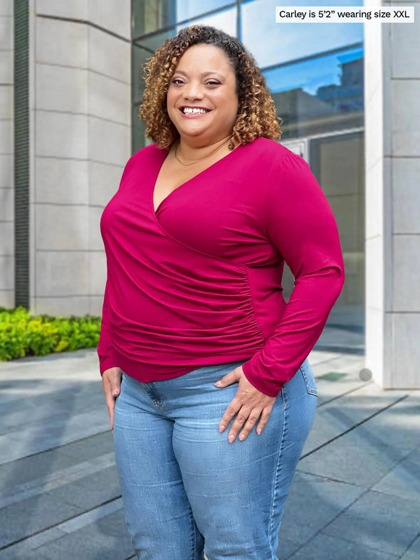 Miik model Carley (5'2", xxlarge) smiling wearing Miik's Kathryn ruched faux-wrap blouse in cerise with jeans