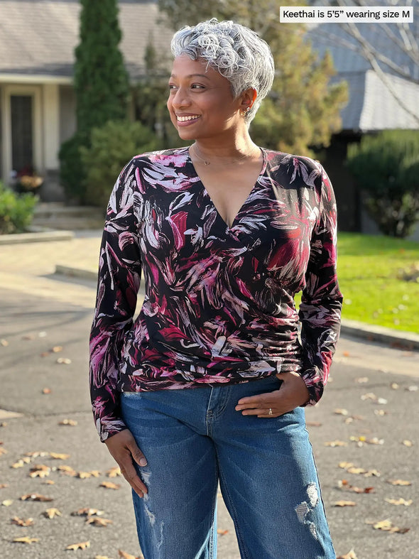 Miik model Keethai (5'5", medium) smiling and looking away wearing Miik's Kathryn ruched faux-wrap blouse in midnight  floral print with jeans #color_midnight-floral