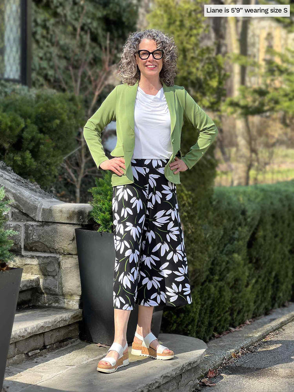 Woman standing in front of a house wearing Miik's Keethai wide leg culotte in floral print, a white top and a green blazer. 
#color_white-lily