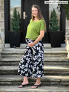 Woman standing in front of a house wearing Miik's Keethai wide leg culotte in floral print and a green top. #color_white-lily