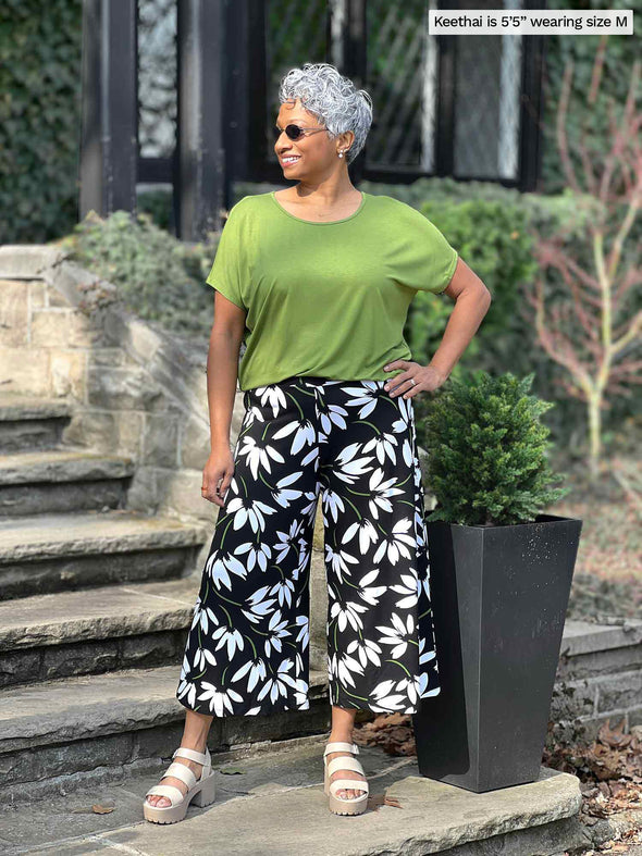 Woman standing in front of a house wearing Miik's Keethai wide leg culotte in floral print and a green top. #color_white-lily