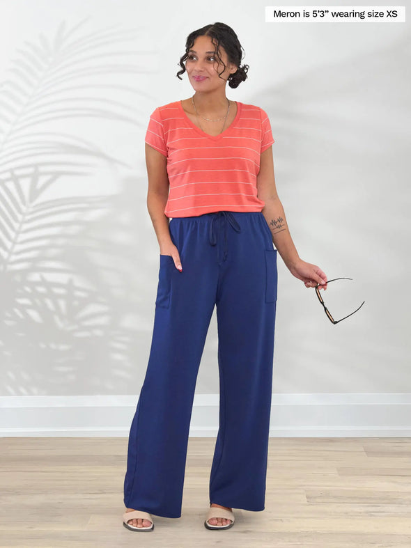 Miik model Meron (5'3", xsmall) smiling and looking away wearing Miik's Kimber french terry wide leg lounge pant in marine bluer with a v-neck tee in papaya pinstripe #color_marine-blue