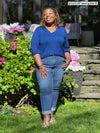 Miik model plus size Erica (5'8", 2x) smiling and looking away wearing Miik's Kimesha v-neck puff sleeve blouse in ink blue with jeans 