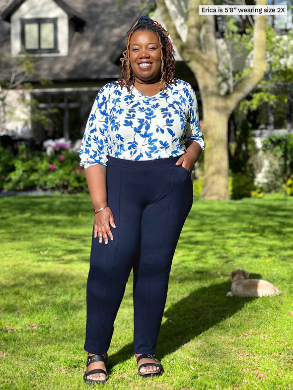 Miik model plus size Erica (5'8", 2x) smiling while standing on a backyard wearing Miik's Kimesha v-neck puff sleeve blouse in ink leaf print tucked in a dress pant in navy 