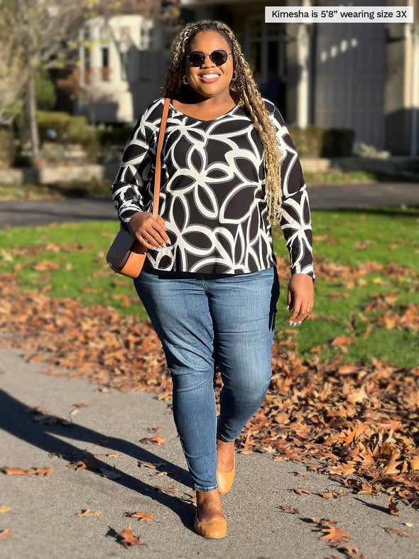 Miik model Kimesha (5'8", 3x) smiling wearing Miik's Kita long sleeve v-neck top in black onyx with jeans and a brown purse #color_black-onyx