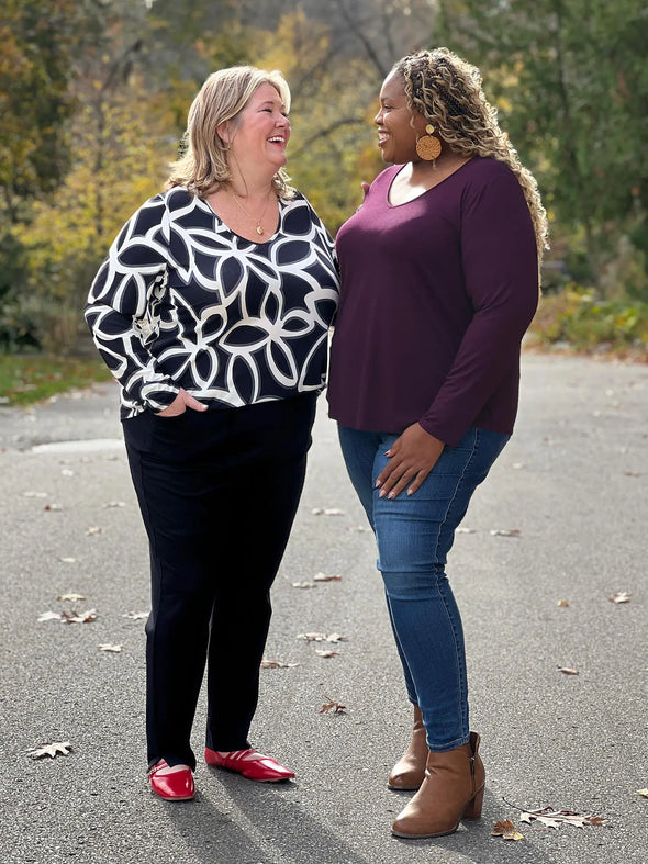 Miik models Kelly and Kimesha (both size 3x) smiling wearing the same top: Miik's Kita long sleeve v-neck top. Kelly is wearing in the black onyx print while Kimesha is wearing in port 