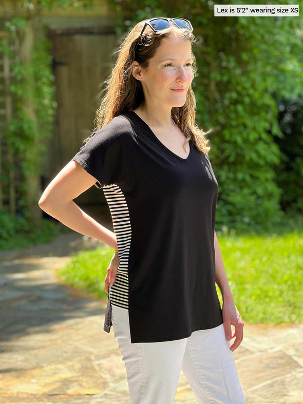 Miik model Lex (5'2", xsmall) smiling while standing sideway wearing Miik's Kylie striped side band top in black mini stripe with a white jens
#color_black-mini-stripe