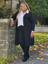 Miik model Kimesha ('8", 3x) smiling wearing Miik's Larissa duster cardigan with pockets in black, plus size, with a collared shirt white and a black dress pant #color_black