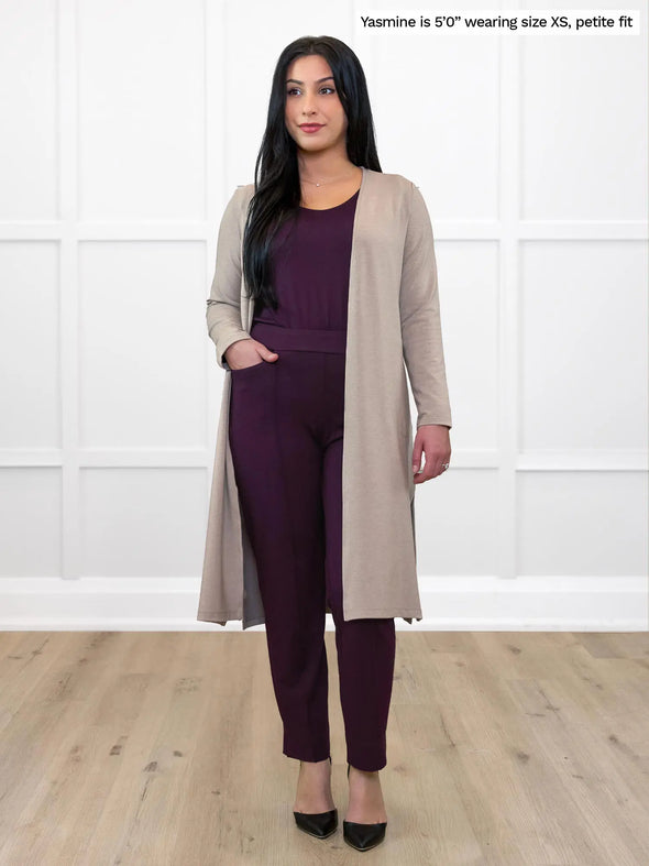 Miik model Yasmine (5'0", xsmall) smiling while standing in front of a white wall wearing Miik's Larissa duster cardigan with pockets in mushroom melange, petite fit, along with an all port outfit #color_mushroom-melange 