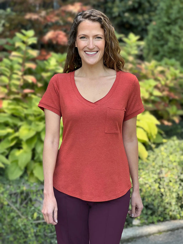 Miik model Lex (5'2", xsmall) smiling wearing Miik's Lex v-neck pocket tee in paprika melange with a dress pant in port purple 