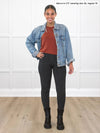 Miik model Meron (5'3", xsmall) smiling while standing in front of a white wall wearing Miik's Lisa2 high waisted legging in charcoal, regular fit, with a chestnut sweater and a denim jacket #color_charcoal 