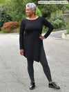 Miik model Keethai (5'5", medium) smiling and looking away wearing an asymmetrical tunic in black with Miik's Lisa2 high waisted legging in charcoal, regular fit. #color_charcoal  