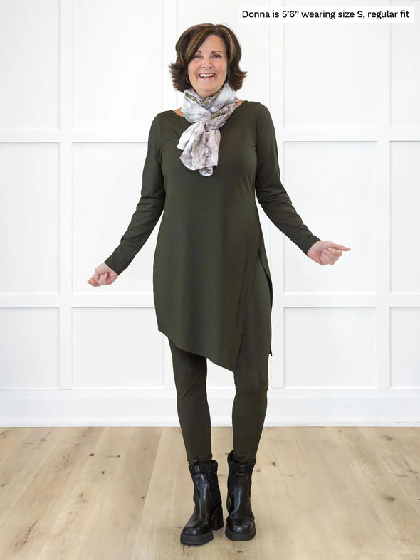 Miik founder Donna (5'6", small) smiling while standing in front of a white wall wearing Miik's Lisa2 high waisted legging in olive, regular fit, with an asymmetrical tunic in the same matching colour and a scarf #color_olive 