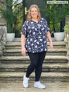 Woman standing in front of a house wearing Miik's Lisa2 high waisted legging in black with a navy floral blouse.