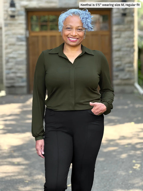 Miik model Keethai (5'5", medium) smiling wearing Miik's Lucia collared shirt in olive, regular fit, with a black dress pant 
#color_olive 