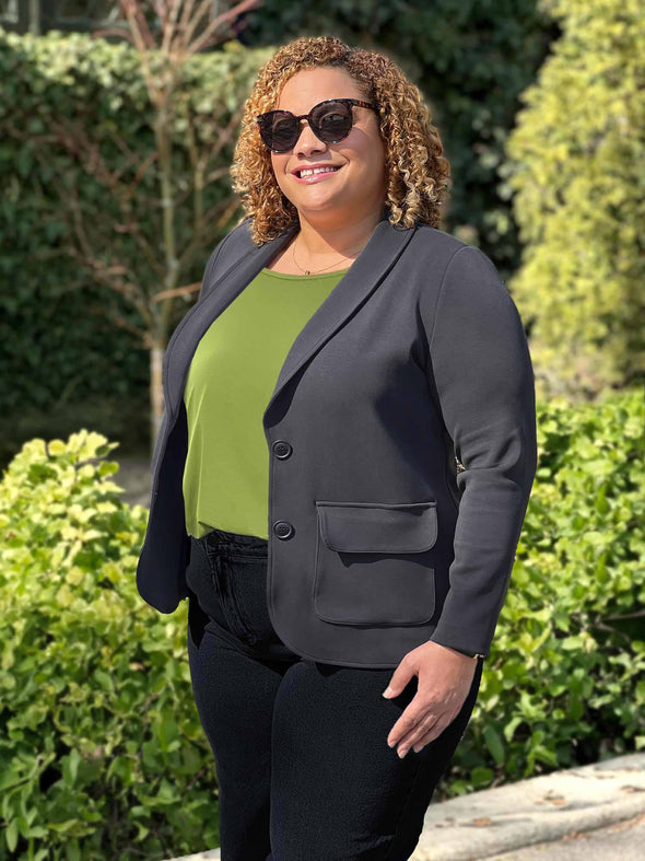 Woman standing in nature wearing Miik's Maeva LightLuxe washable blazer in graphite grey over a green top and black pants
#color_graphite