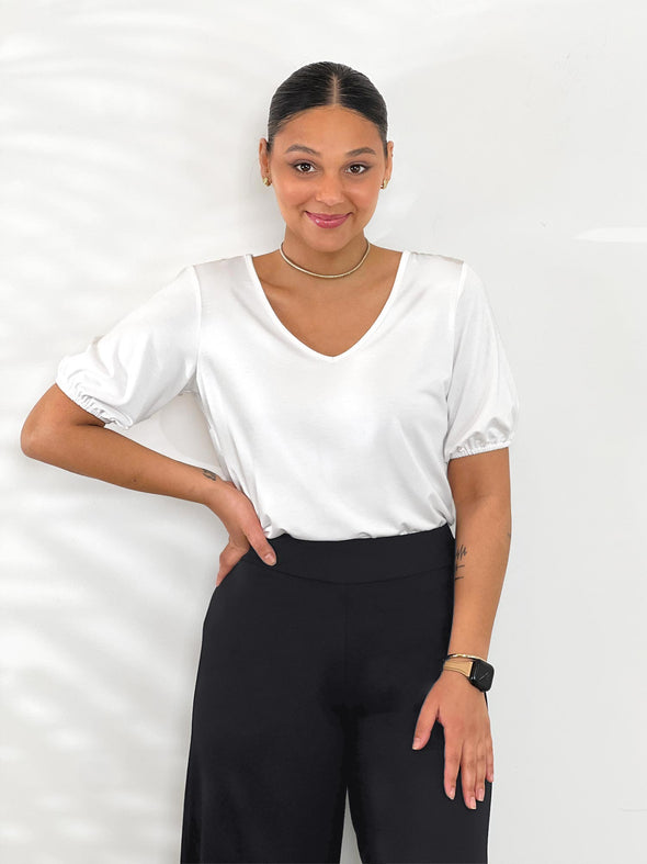 Miik model Meron (5'3", xsmall) smiling wearing Miik's Makena v-neck puff sleeve blouse in white tucked in a black pant 
#color_white