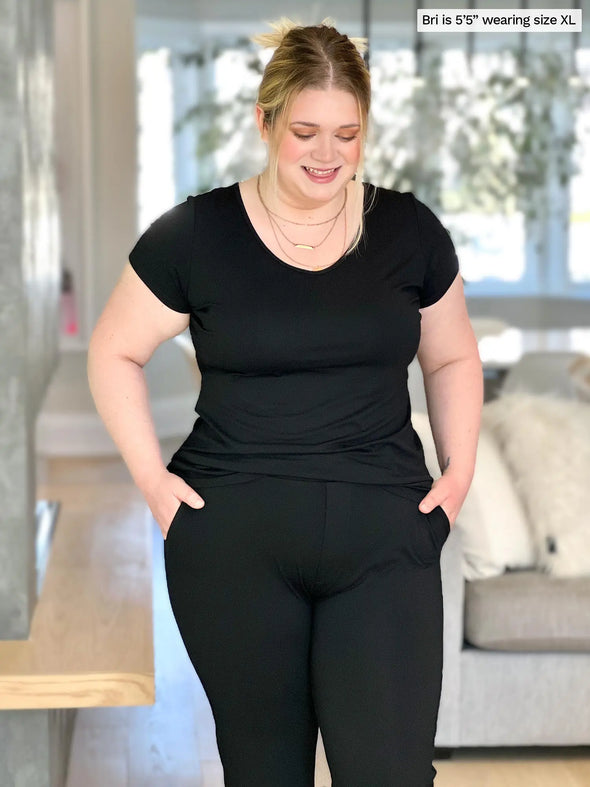 Miik model Bri (5'5", xlarge) smiling and looking down wearing Miik's Marianna reversible classic tee in black with a matching color pant 
#color_black 